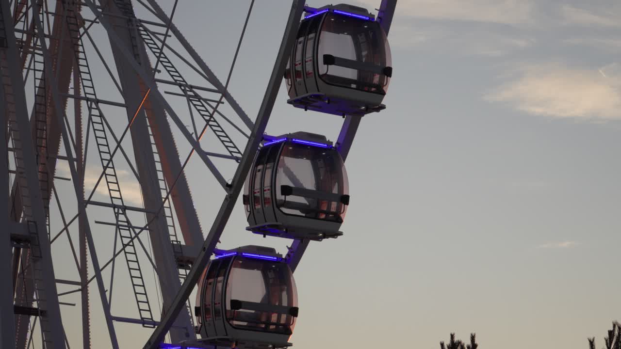 Primo piano di cabine illuminate di una ruota panoramica che ruotano al tramonto sulla Costa d'Opale in Francia, contro un morbido cielo serale.