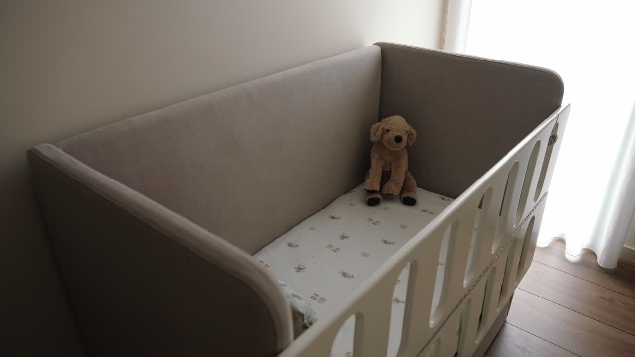 Baby crib with soft mattress, decorated with a teddy bear and sunlight coming through the window