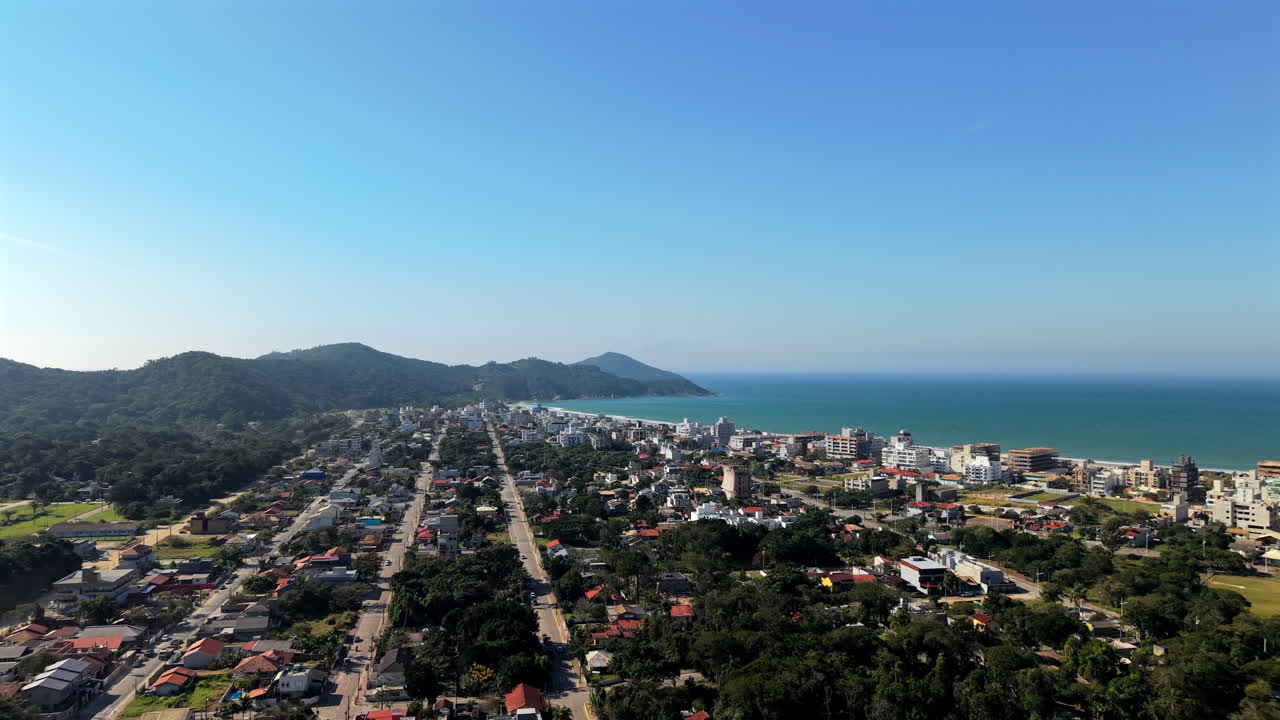 Sorvolo panoramico con drone del quartiere urbano con strade che conducono alla costa della spiaggia di Mariscal, Bombinhas, Santa Catarina, Brasile