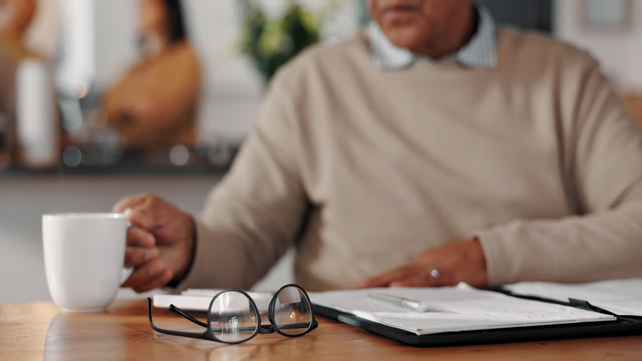 hombre sentado en una mesa, escribiendo en un cuaderno con una taza de café a su lado