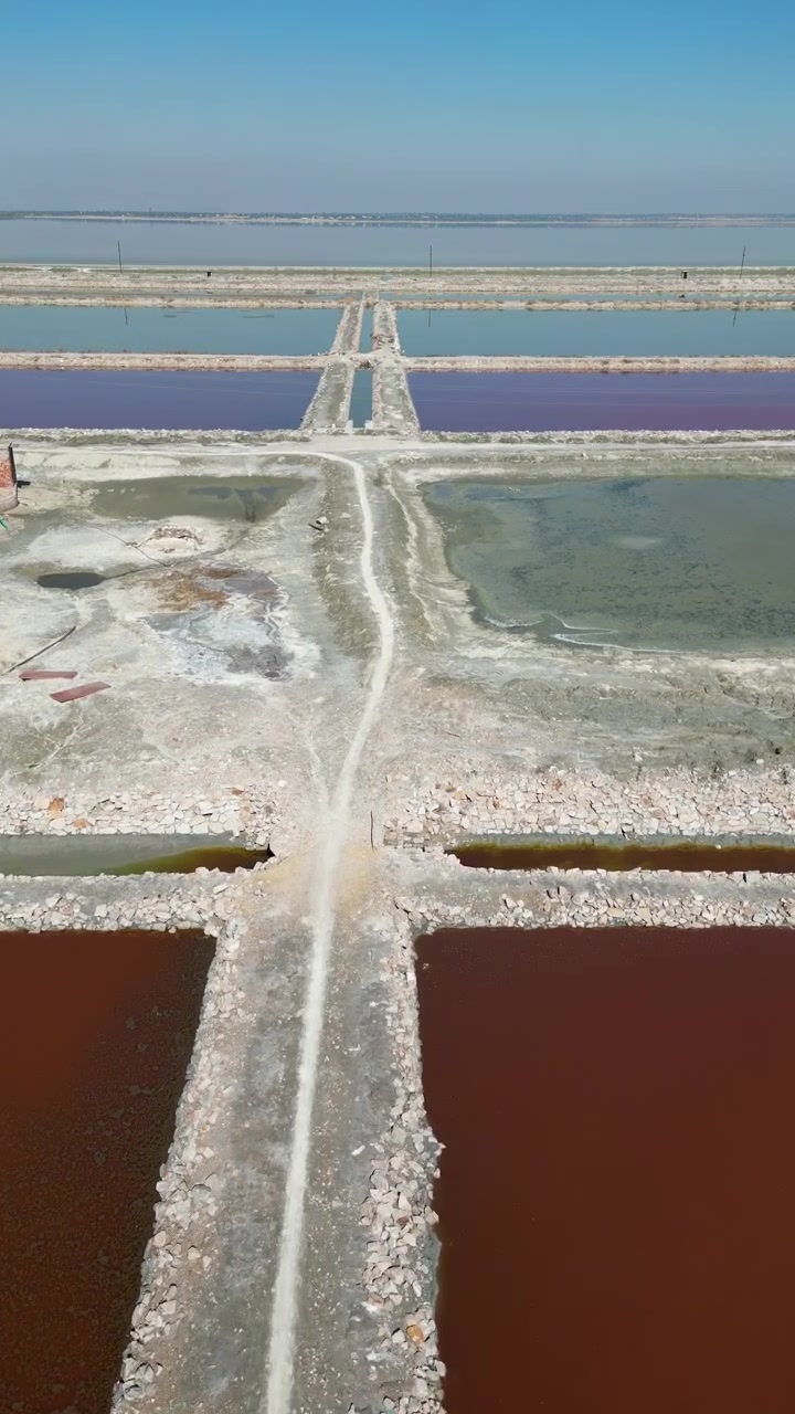 Cinematic aerial shot of colorful salt evaporation ponds and geometric patterns at Sambhar Salt Lake, showcasing sustainable mineral extraction and unique landscape textures.