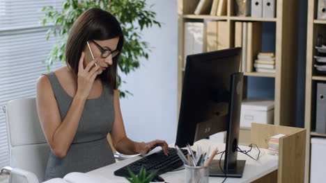 pregnant businesswoman in glasses working at the computer in the office and talking on the phone 1