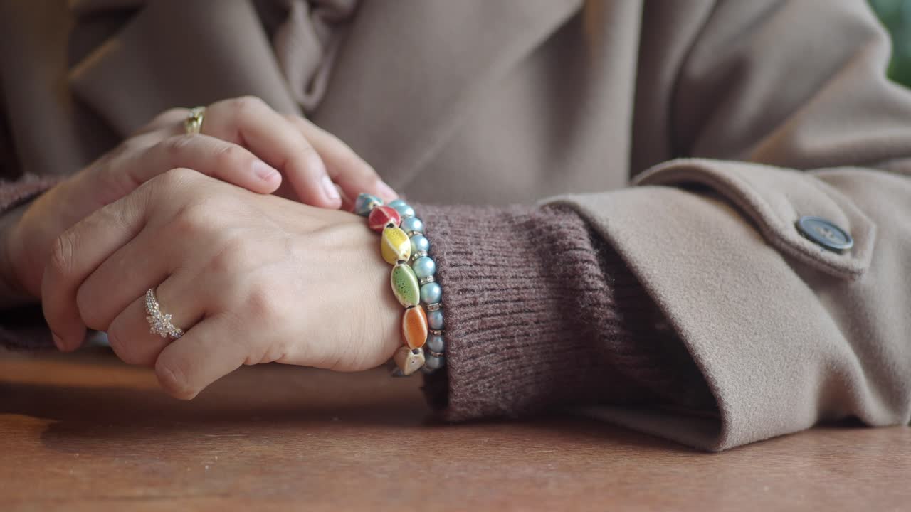 Close-Up of Woman's Hands with Colorful Bracelets on a Wooden Table