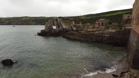 Vista-Aérea-Inversa-Descendiendo-Bajo-En-Traeth-Porth-Wen-Beach-Bay-Sitio-De-Ladrillo-Abandonado-En-La-Costa-Del-Mar-Irlandés