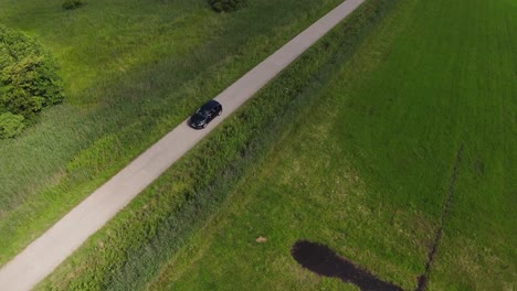 drone shot of a small black car driving over a small stone path between fields