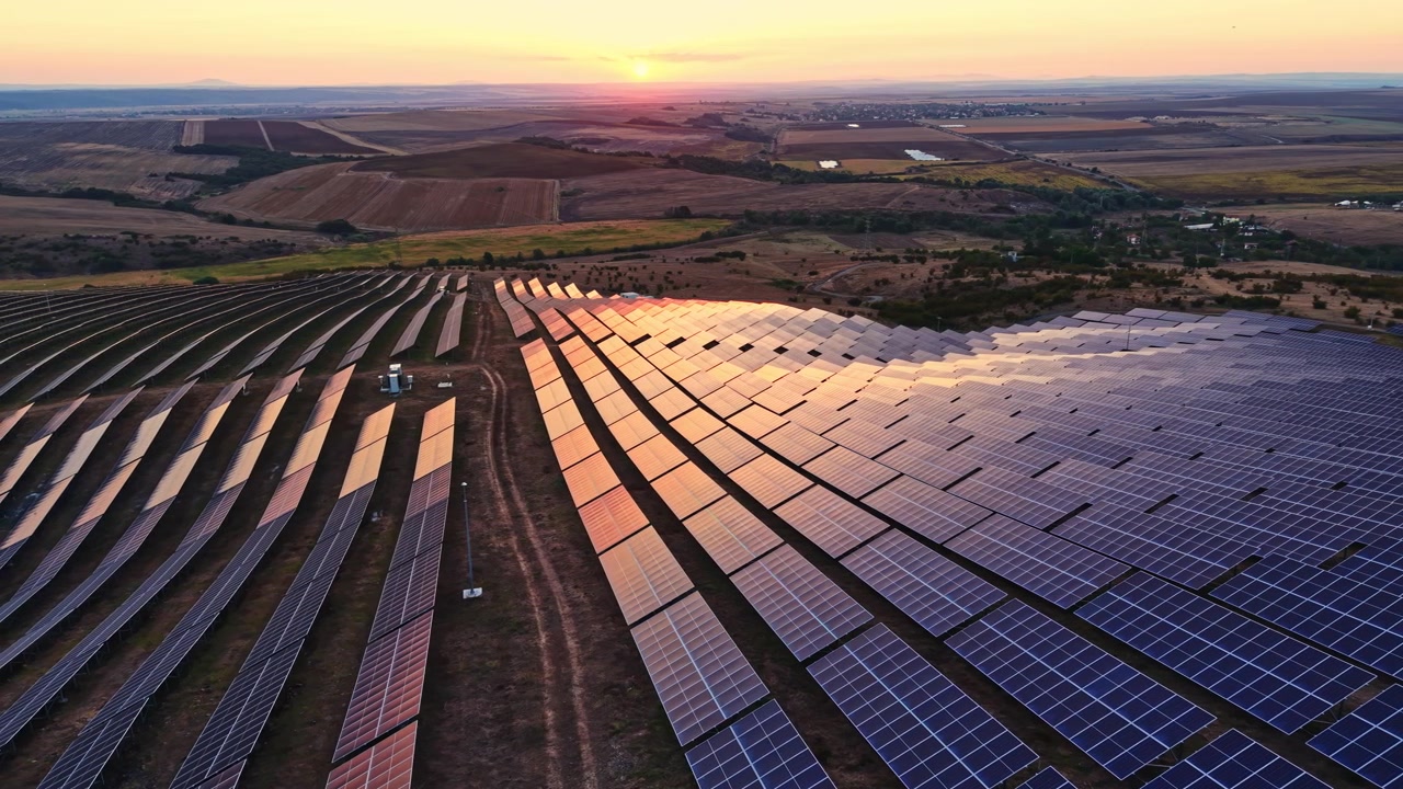 Solpaneler dækker et område ved solnedgang i et stort åbent landskab omgivet af marker og bakker