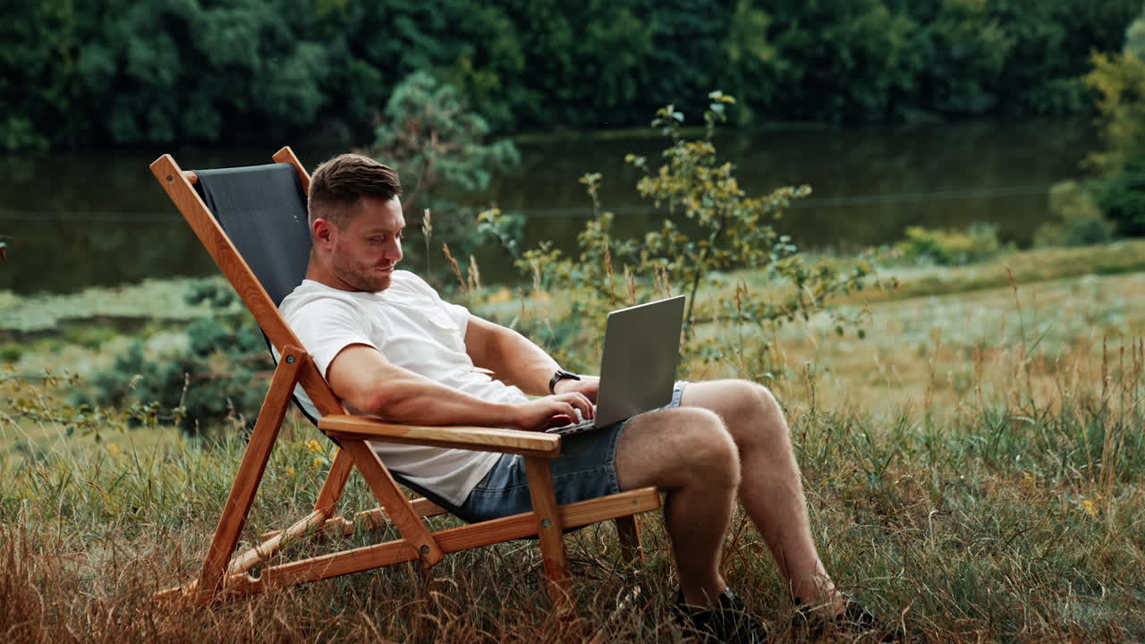 Man sitting peacefully in the chair among the nature. Freelancer types on his laptop working remotely.