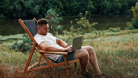 man sitting peacefully in the chair among the nature. freelancer types on his laptop working remotely.