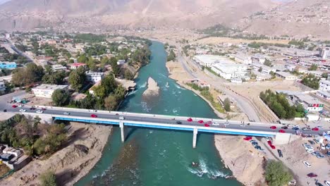 Eine-Luftaufnahme-Von-Zwei-Brücken,-Die-Einen-Fluss-In-Einem-Dorf-überqueren,-Mit-Autos,-Die-Die-Brücke-überqueren