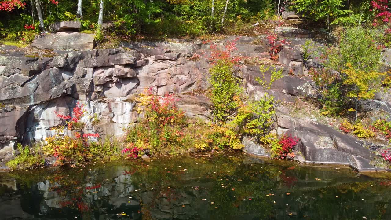 Flying over rocky coast of lake and its colorful vegetation in Reserve Faunique La V&eacute;rendrye
