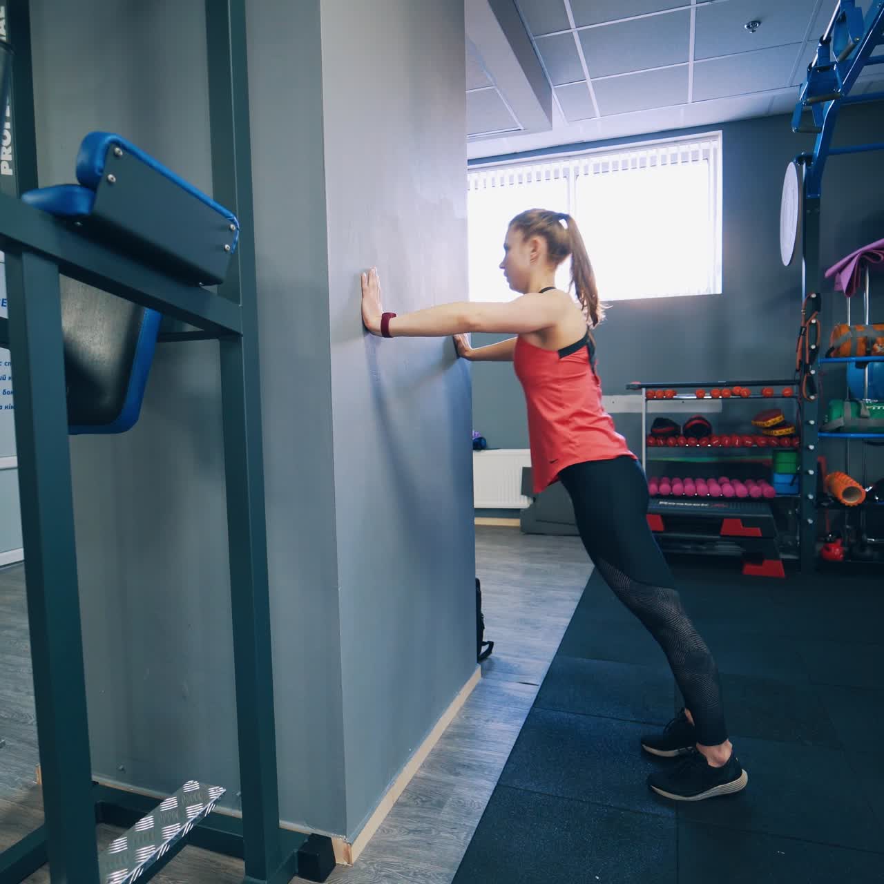Daily workout. Side view of a slim girl training indoors. Young woman standing and doing push-ups from the wall in the modern fitness centre.