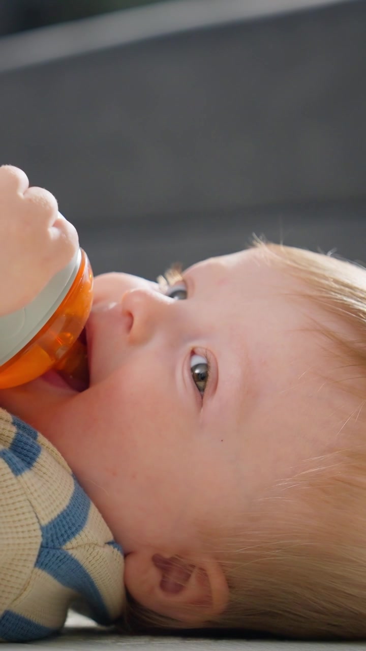 Bambino sdraiato che beve da un bicchiere con beccuccio