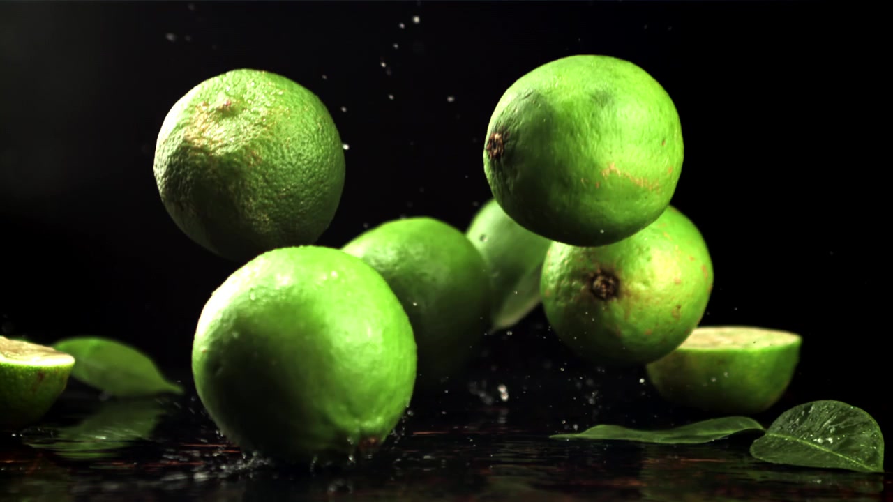 Limas Verdes Frescas Caindo e Espirrando Água em Câmera Lenta