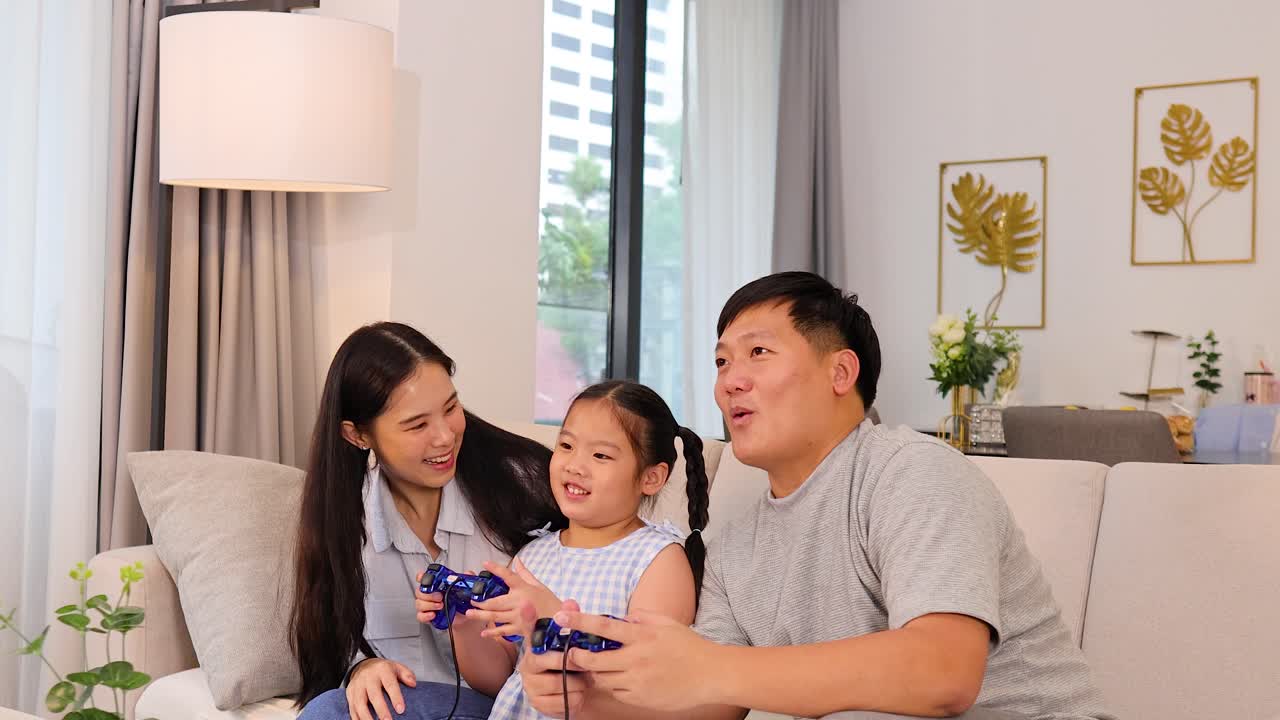 明るい自然光の下、親と子供がソファーでビデオゲームを楽しみ、陽気でリラックスした雰囲気。