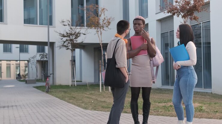 Gruppo di amici multiculturali che parlano distratti fuori da un campus universitario.