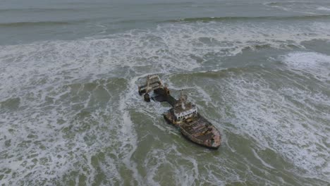 waves crashing on destroyed marine vessel shipwreck in namibia, aerial