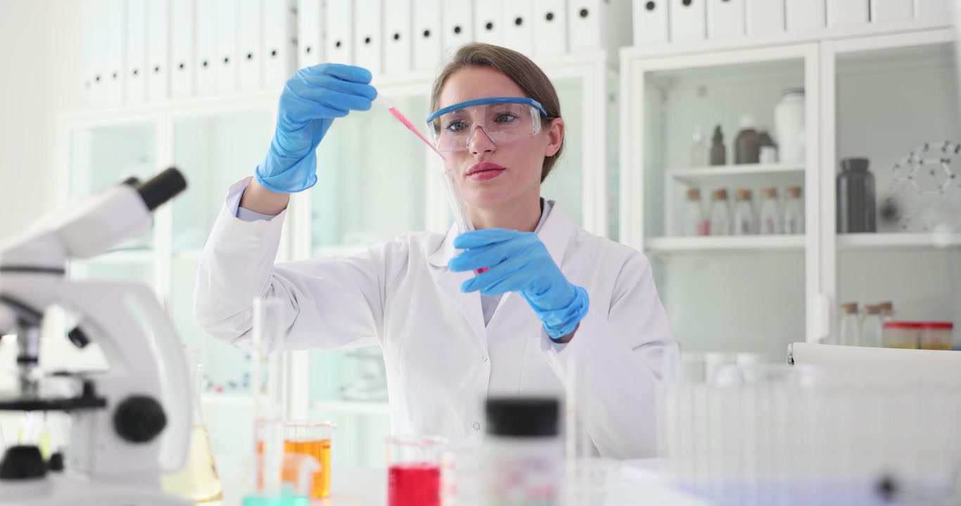 Chemist pours bright liquid into test tube using pipette