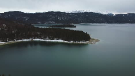 Scenic-4K-UHD-drone-aerial-view-upon-Bavaria's-idyllic-lake-Walchensee-with-its-particular-blue-water-and-islands-in-the-rural-Bavarian-countryside-with-a-beautiful-blue-sky-and-the-alps-mountains