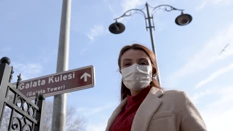 beautiful girl wearing protective medical mask and fashionable clothes does heart shape with hands at galata tower sign background