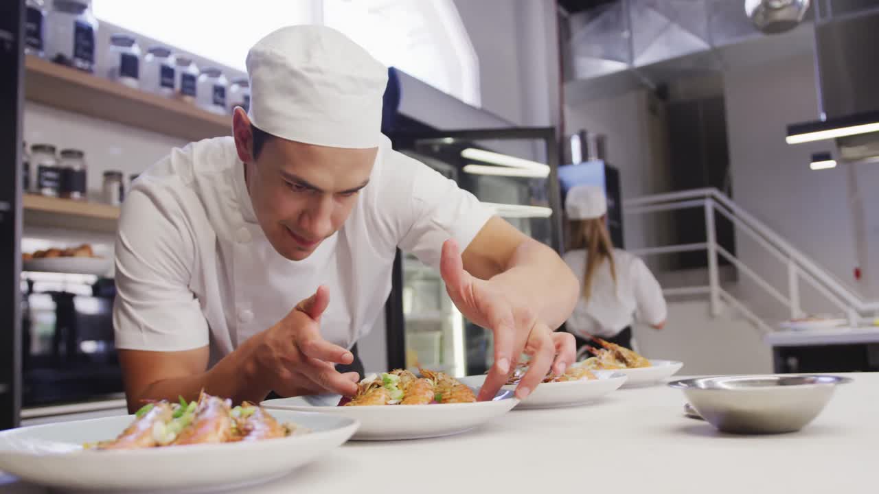 cocinero de raza mixta vestido con ropa blanca en una cocina de restaurante, poniendo comida en un plato