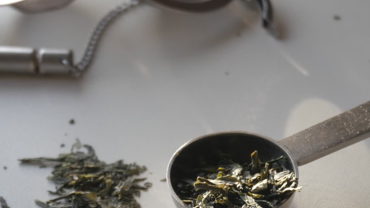 Fresh green tea leaves in a metal spoon, showcasing their vibrant, raw form