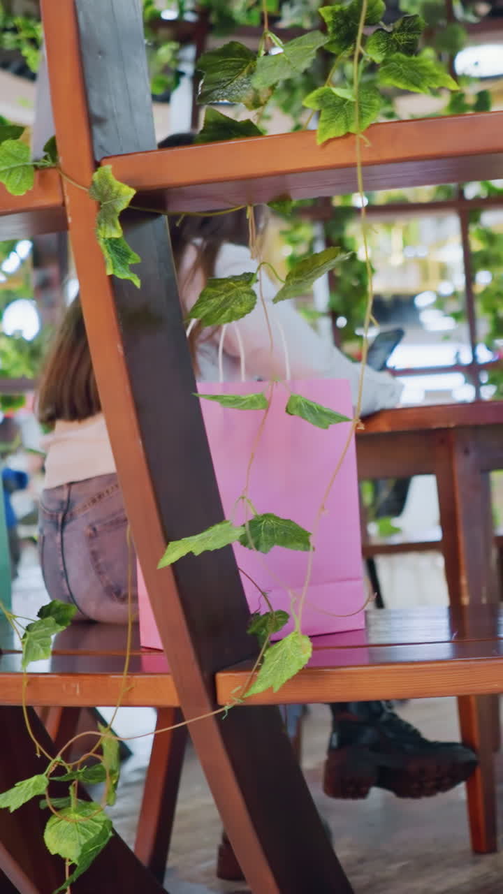 장식 된 나무 좌석에 앉아있는 젊은 성인, 에 전화, 쇼핑 가방을 들고, 사람들은 역동적인 조명과 함께 활기차고 바쁜 쇼핑몰에서 돌아다니는 것을 볼 수 있습니다.