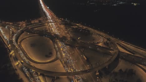 illuminated complex highway junction and cars traffic jam at winter night. drone is orbiting, camera is tilting down. aerial view. establishing shot.