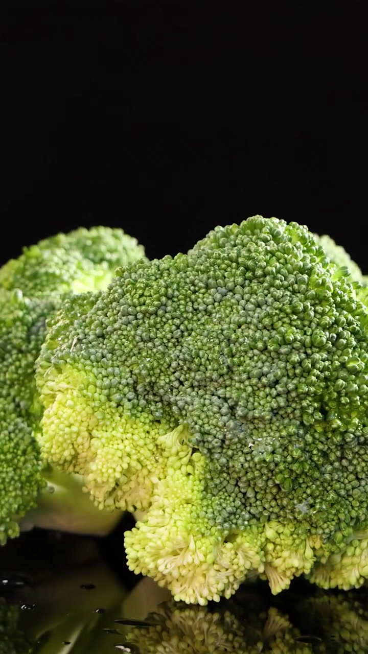 Cimette di broccoli ruotano fluidamente sotto una brillante illuminazione da studio, evidenziando texture verdi vibranti su uno sfondo nero lucido con un movimento di telecamera fluido