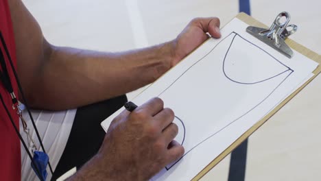 Male-african-american-basketball-coach-using-notebook-in-indoor-court,-in-slow-motion