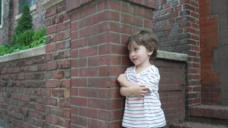 Retrato-De-Un-Niño-Pequeño-Con-Las-Manos-Cruzadas-De-Pie-Contra-La-Pared-De-Ladrillo-Rojo-En-Un-Día-Soleado