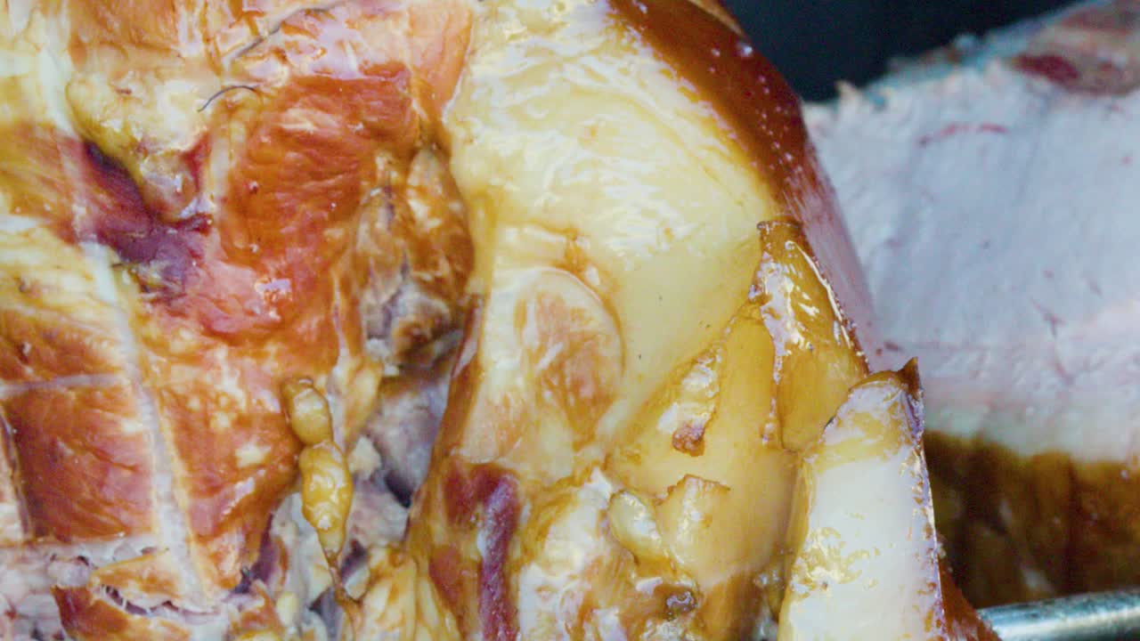 Juicy pork knuckle slowly rotates on spit, golden brown, close-up, natural daylight, outdoor market