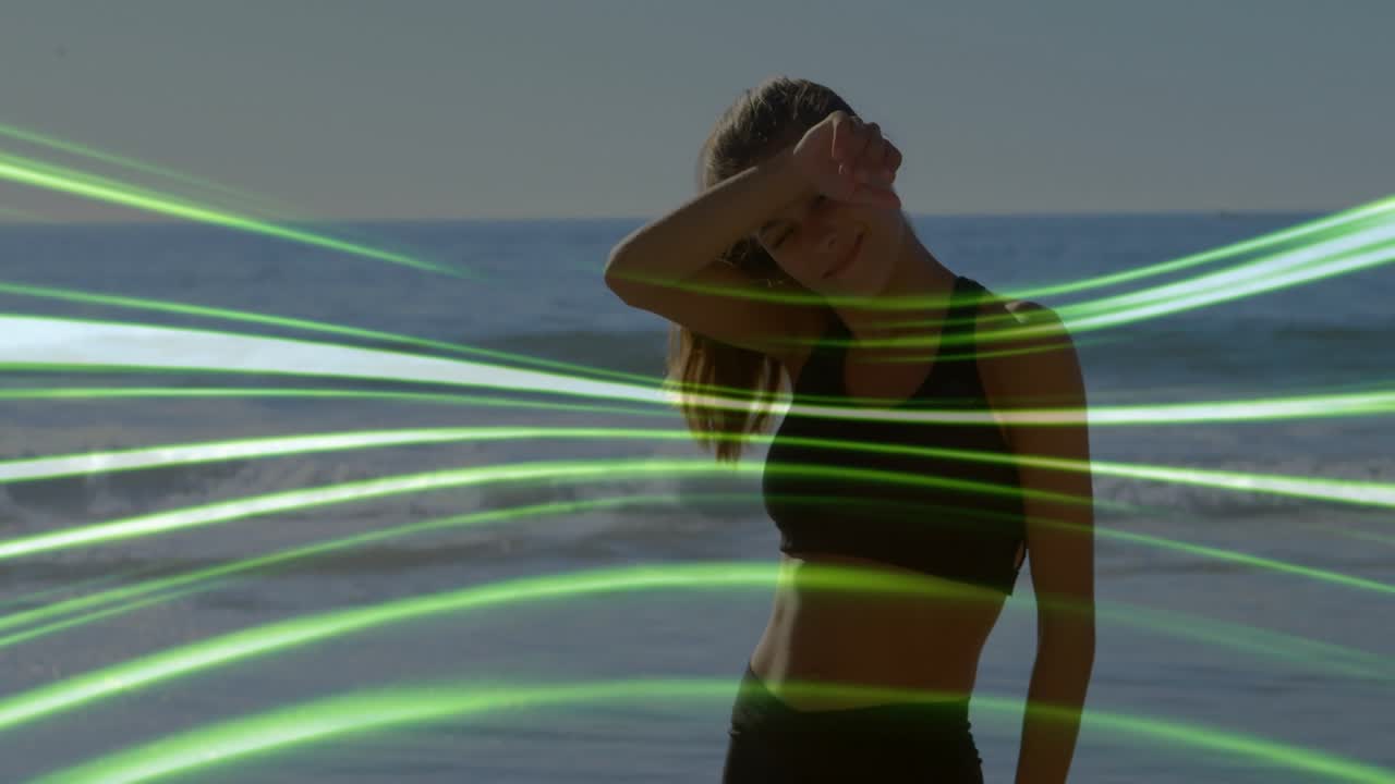 Mulher se ajeitando, protegendo os olhos na praia enquanto a câmera sobe, fitas verdes cruzando o corpo para moda
