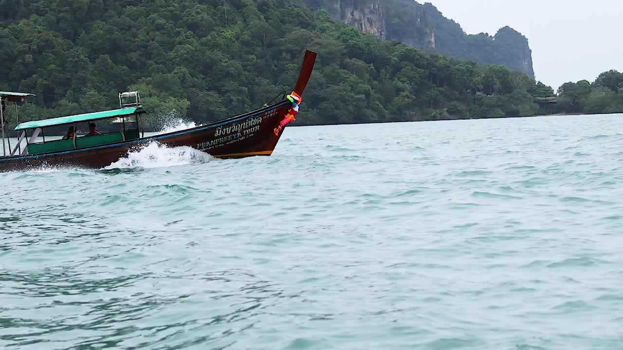 A long-tail boat navigates tranquil waters with lush green islands in the background.