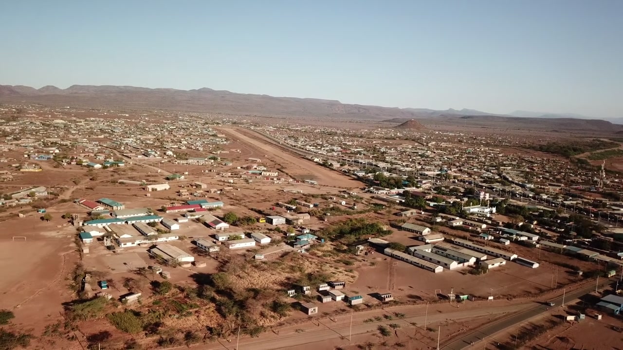 Aerial panorama of Kakuma, Turkana County, Kenya, showing the settlement spreading across an arid landscape with a central roadway or airstrip.