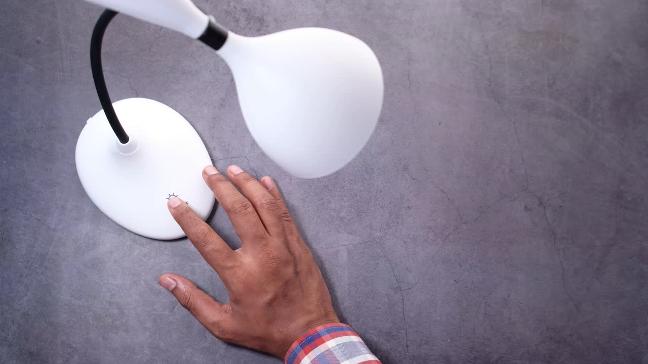 mano tocando el interruptor de una lámpara de mesa blanca