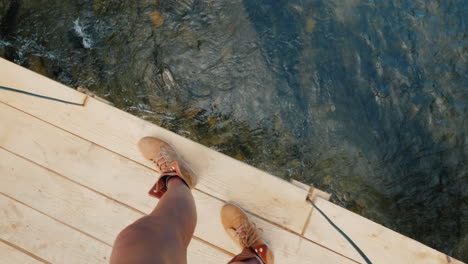 a man in trekking boots walks along the edge of a wooden bridge over the precipice pov video