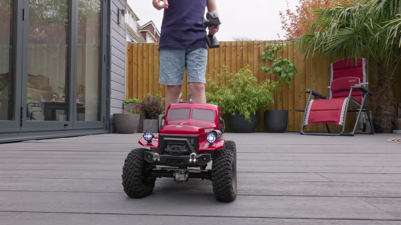 Giovane ragazzo a casa all'aperto in giardino che gioca con la sua auto RC, camion e 4x4.