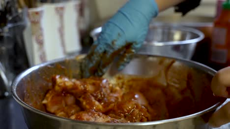 mano en guante azul mezclando pollo en marinada, telón de fondo de la cocina, primer plano