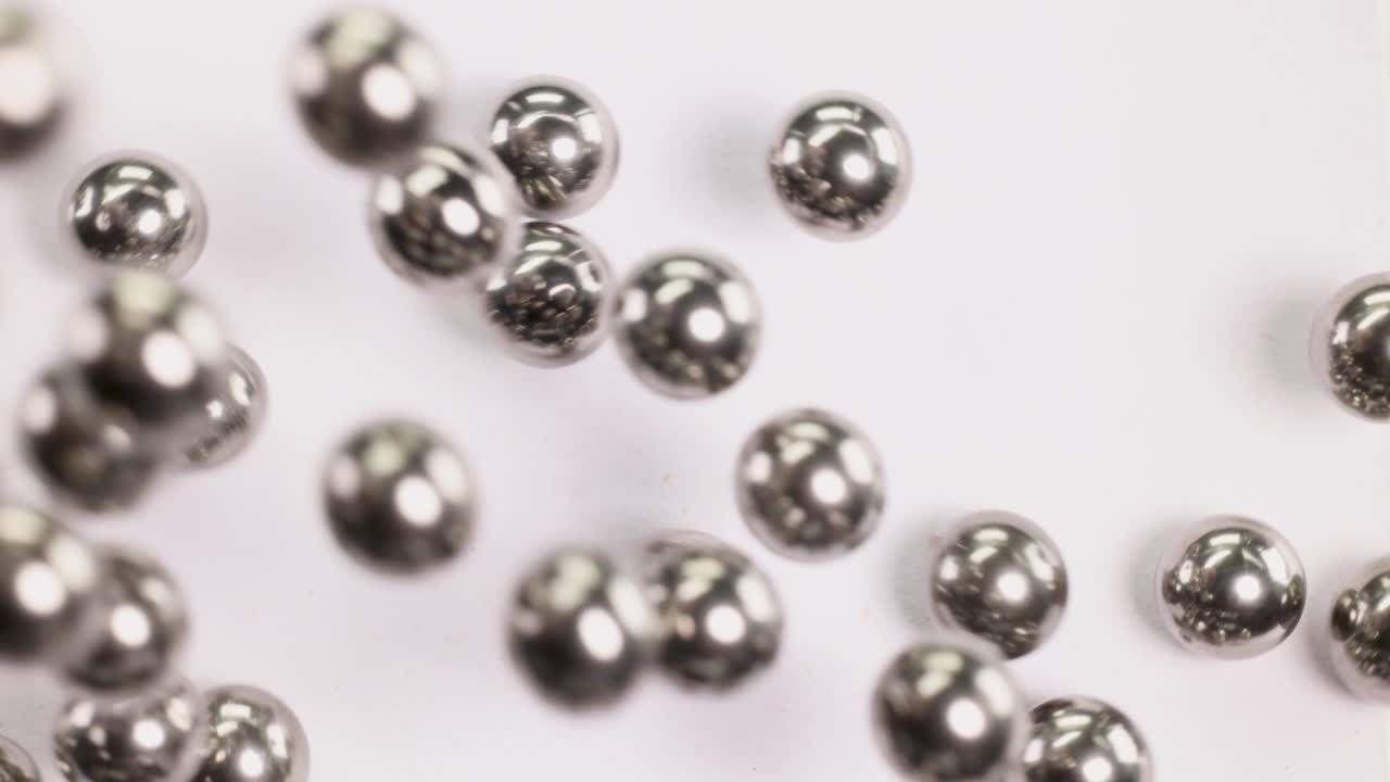 Close-up of metallic ball bearings rolling across a white surface, showcasing their reflective surfaces and dynamic movement