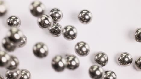 close-up of metallic ball bearings rolling across a white surface, showcasing their reflective surfaces and dynamic movement