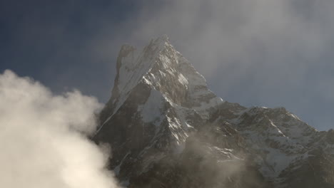 a view of fishtail or machhapuchhare mountain in the morning light with the fog and clouds passing by in front of the snow covered peak
