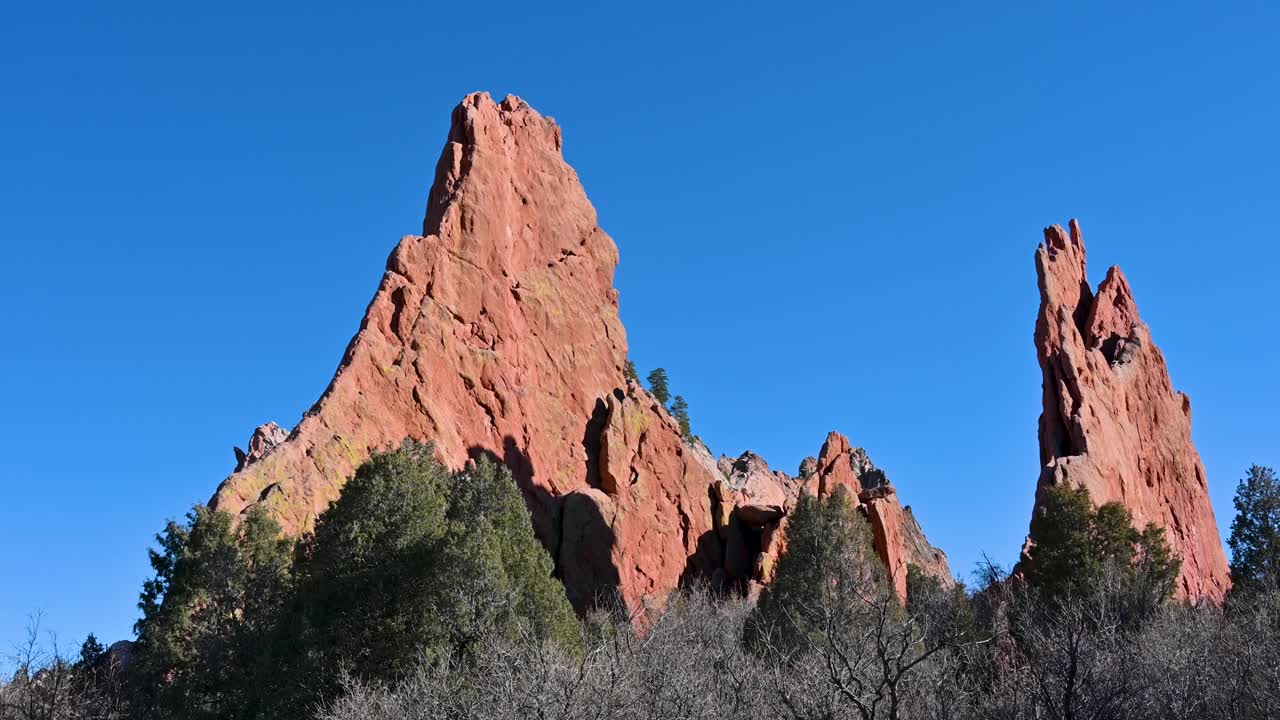 Drone footage of towering red sandstone spires framed by evergreens at Garden of the Gods, Colorado, under clear blue skies