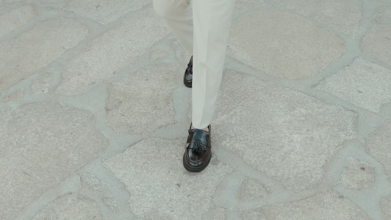 stylish man walking on stone pavement wearing polished black loafers and white trousers