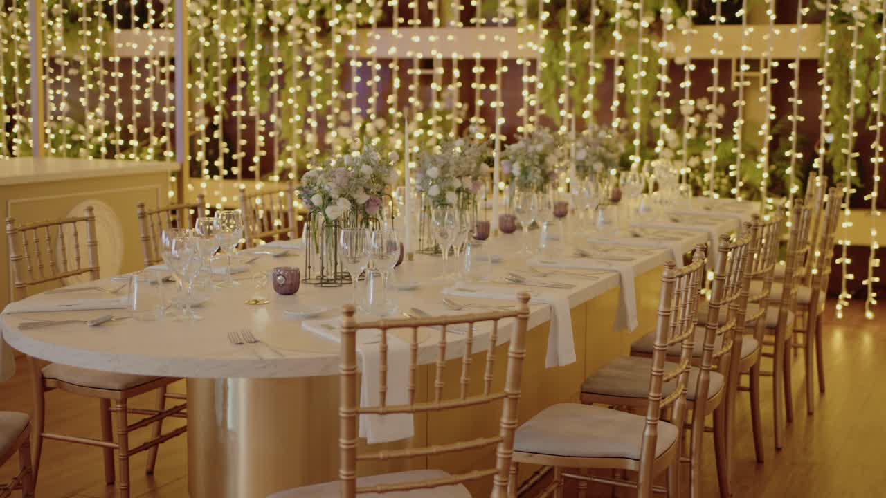 elegant banquet table adorned with delicate floral centerpieces, surrounded by gold chairs, and softly illuminated by cascading fairy lights, creating a warm and romantic atmosphere