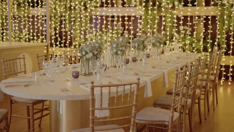 elegant banquet table adorned with delicate floral centerpieces, surrounded by gold chairs, and softly illuminated by cascading fairy lights, creating a warm and romantic atmosphere
