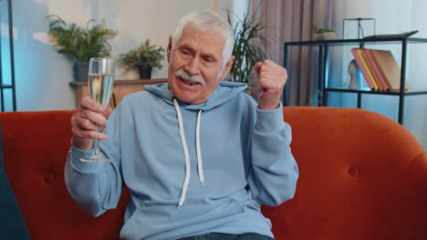 joyful senior old grandfather hold glass of champagne cheering, drinking, celebrating success win