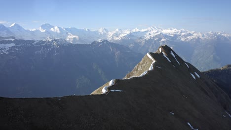 Man-hiking-on-beautiful-ridge-top-amongst-huge-mountains-and-above-a-green-valley-with-a-blue-lake