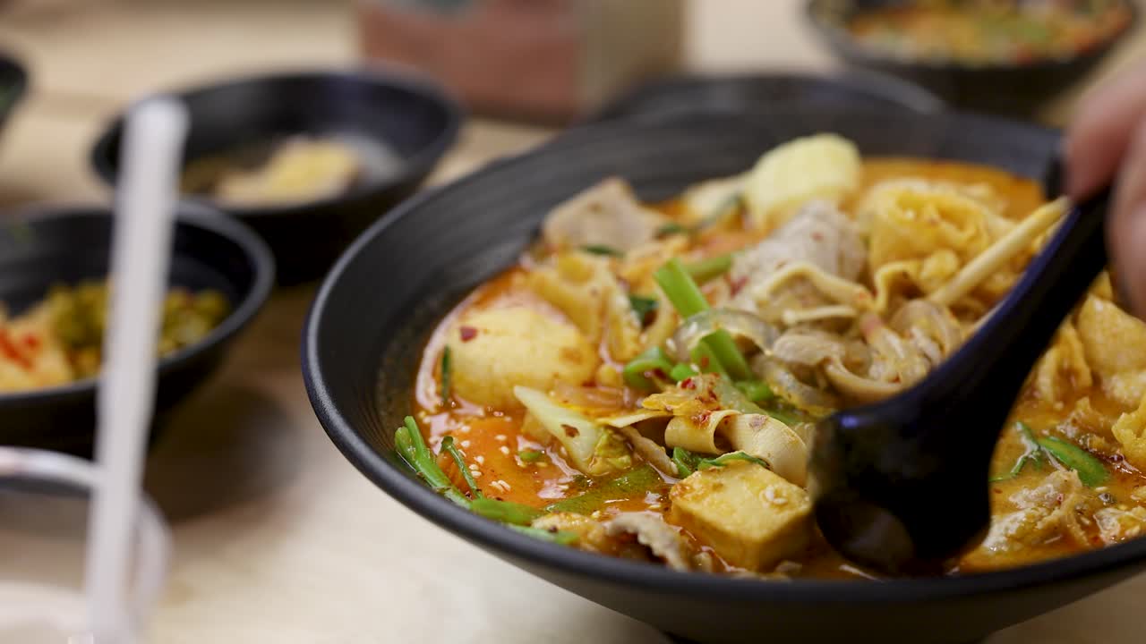 Hand stirs hearty Asian hotpot with tofu, meat, and vegetables in bright, close-up setting