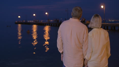 una pareja de ancianos enamorados en el paseo marítimo por la noche.