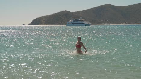 cheerful woman in bikini jumping in the sea on a sunny summer day with yacht in background